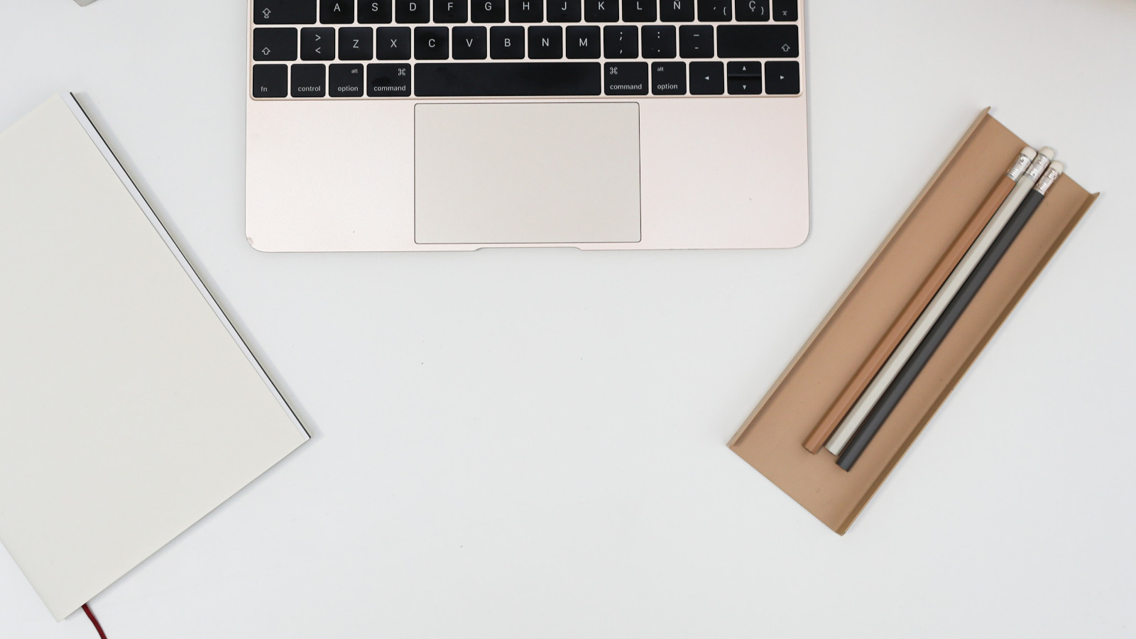 A laptop computer, a notebook and pencils laid out on a desk